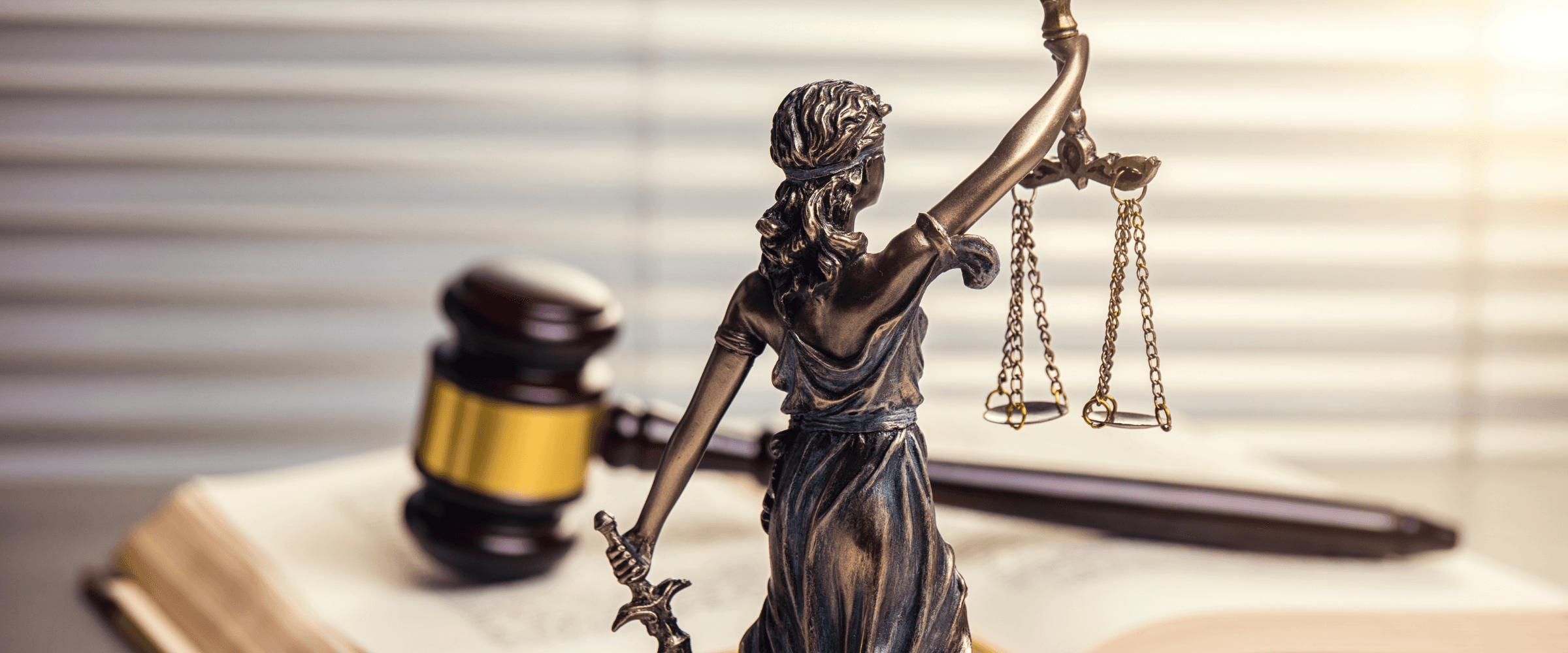 Lady Justice and a gavel on a book siting on a desk.