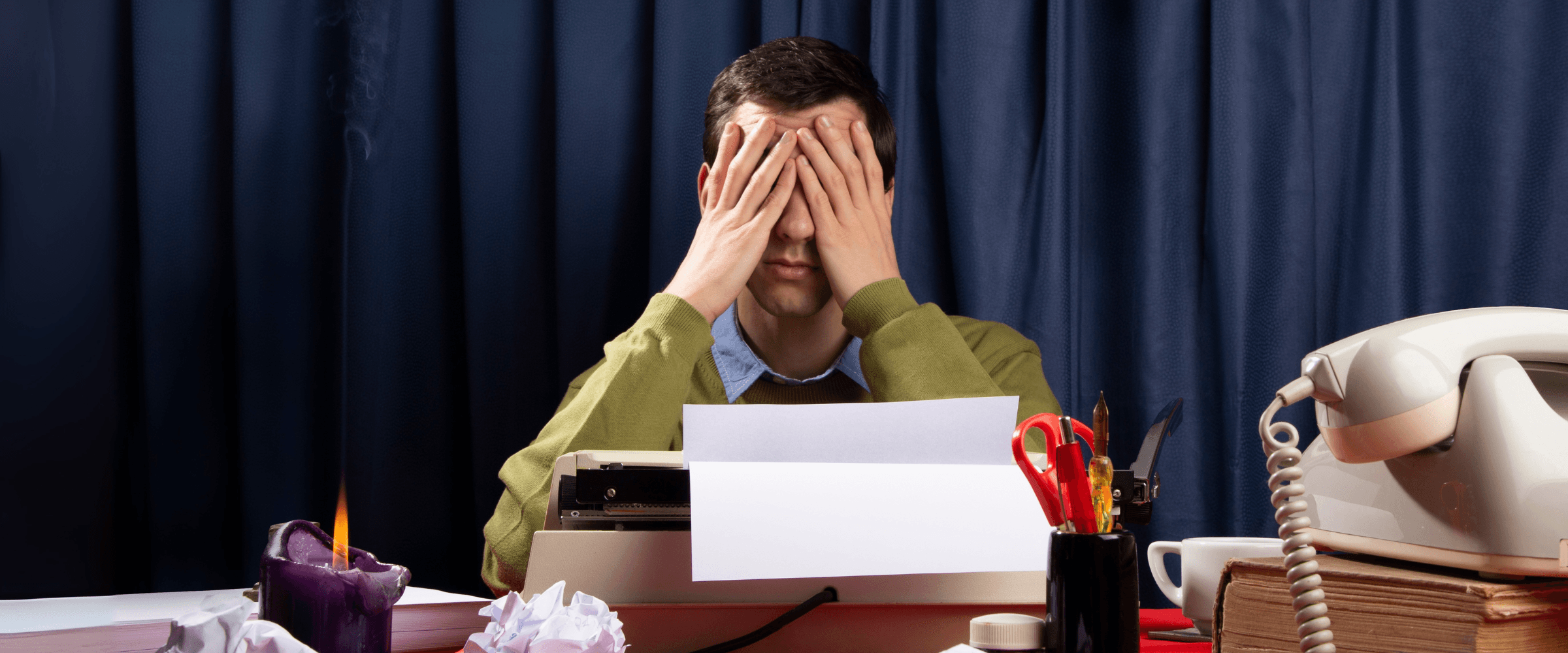 Man holding his face in frustration over his cluttered desk